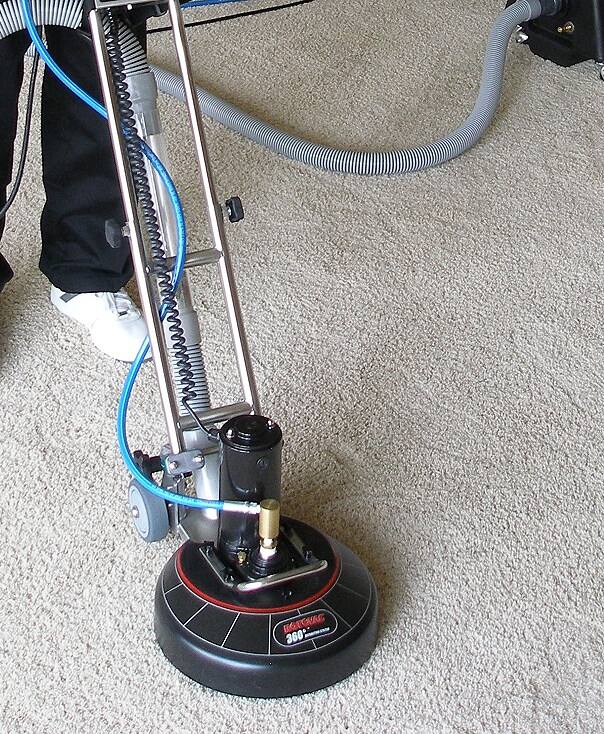 Rotary carpet cleaning machine working on a beige carpet